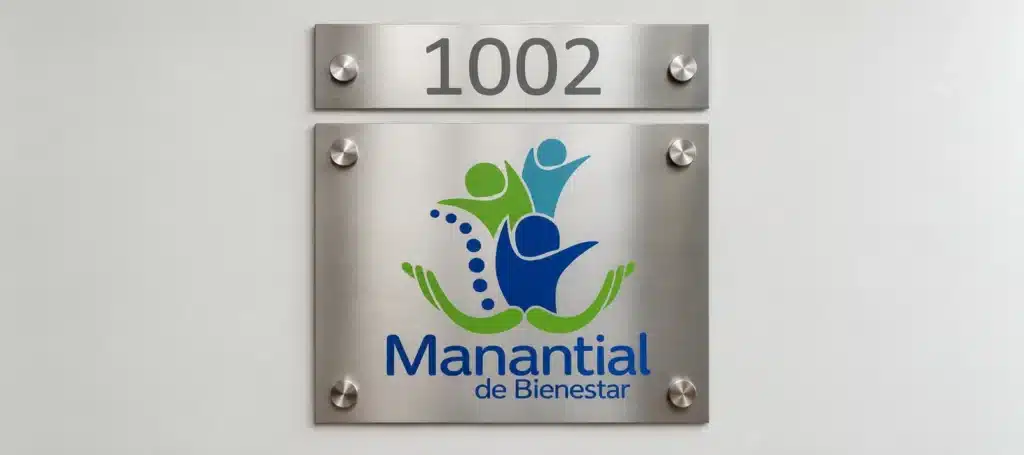 Placa de acero cepillado con número 1002 y logo de salud fijada con separadores sobre pared clara