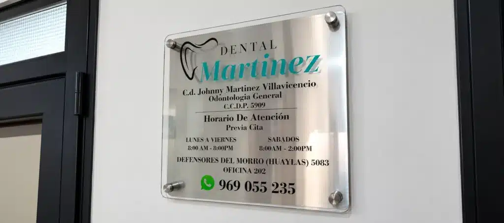 Placa de acrílico transparente con datos de consultorio dental fijada en pared de pasillo