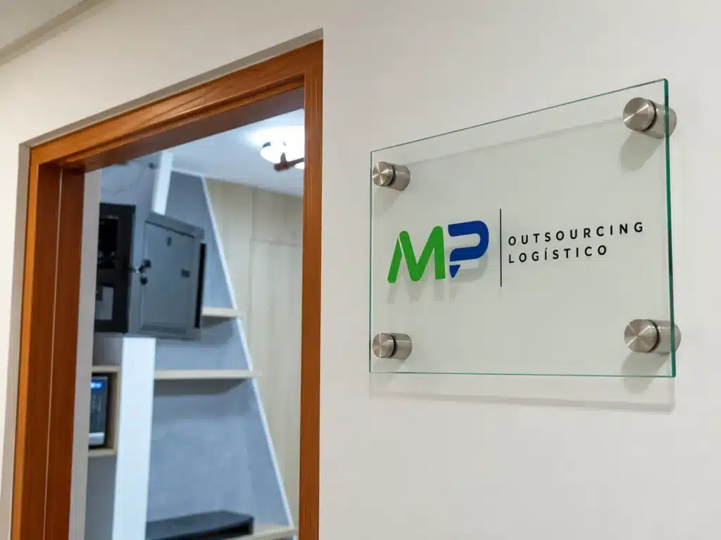 Placa de vidrio transparente con logo corporativo fijada con separadores metálicos junto a una puerta de madera